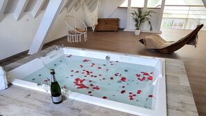 A spacious room with a large bathtub filled with rose petals, a hanging chair, and a wooden bench.