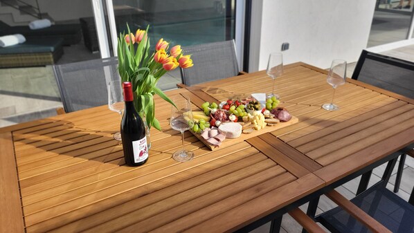 A wooden table with a bottle of wine, a glass, a bouquet of tulips, and a charcuterie board with various cheeses and fruits.
