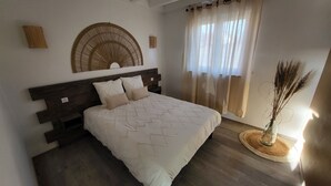 Une chambre à coucher comprenant un lit, une tête de lit, un élément décoratif fixé au mur, une fenêtre avec des rideaux et un vase contenant des plantes séchées.