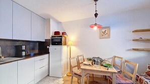 A compact kitchen with white cabinets, a refrigerator, a coffee maker, and a dining table with chairs.