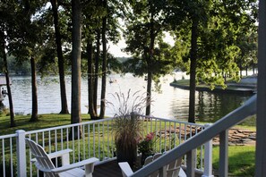 A deck with chairs overlooking a lake, surrounded by trees. - Lake Sara cottage: 3BR/2BA, hot tub, swim dock, firepit, kayaks, & lake views! (Effingham)