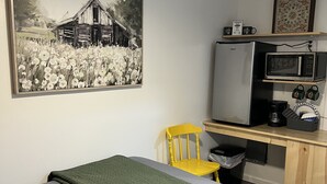 A bedroom with a bed, a desk with a microwave, a chair, and a painting on the wall. - Quaint Cabin #7 - Pymatuning Lake (Jamestown)