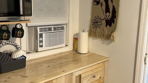 A kitchen with a microwave, toaster, and kettle on the countertop. There is a wooden cabinet below the counter and a wall-mounted shelf above it. - Quaint Cabin #7 - Pymatuning Lake (Jamestown)