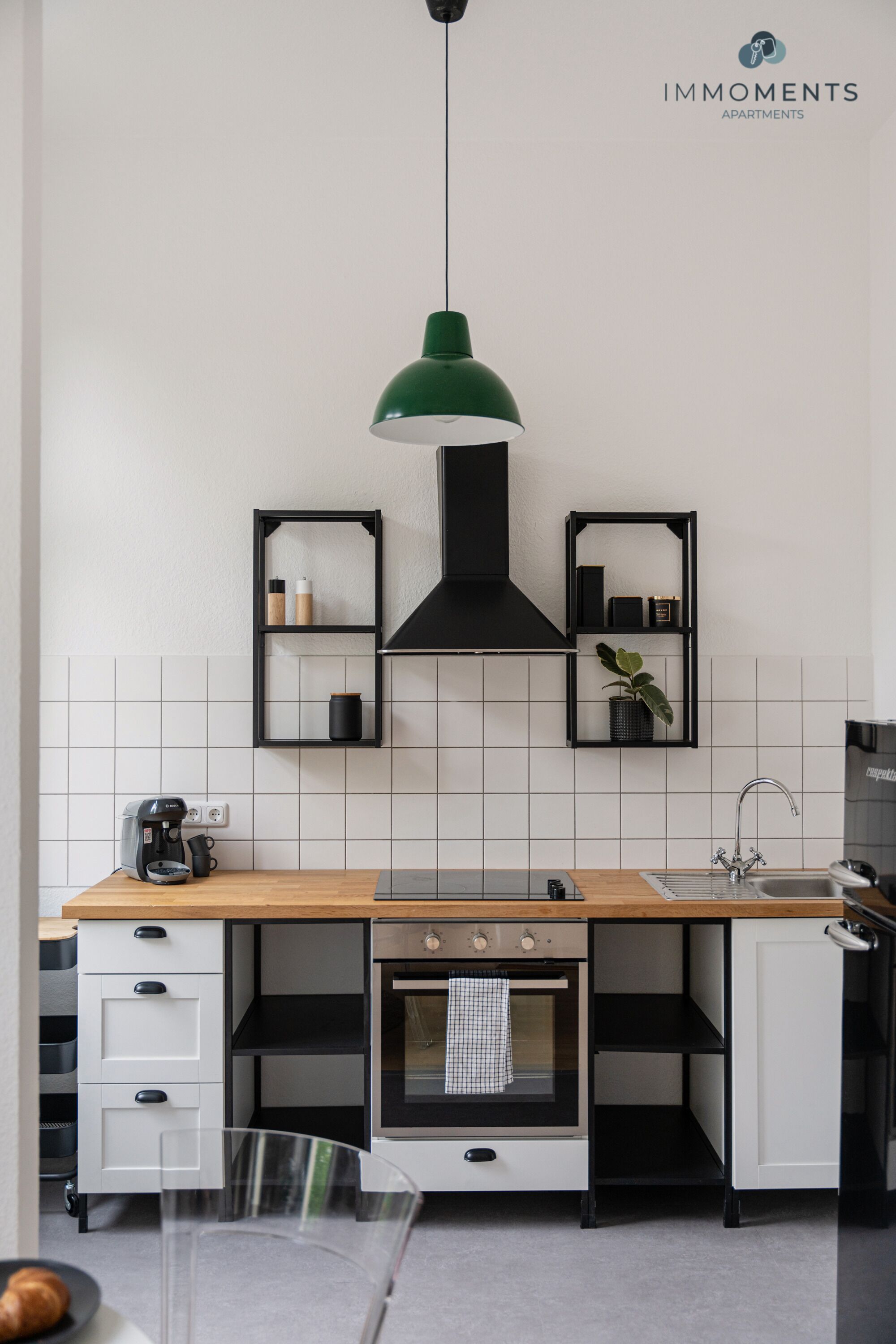 Eine moderne Küche mit einer Holz Arbeitsplatte, einem eingebauten Backofen, einer Kaffeemaschine und schwarzen Regalelementen.
