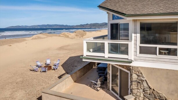 Ein direkt am Strand gelegenes Anwesen mit einem Balkon mit Meerblick, einer Terrasse mit Stühlen und einer Steinmauer.