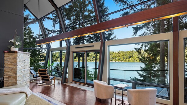 Un intérieur moderne avec de grandes fenêtres, une cheminée en pierre et des sièges placés près des portes vitrées.