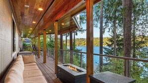 Une terrasse en bois dotée d’un foyer intégré et d’un espace salon offrant une vue sur un lac.