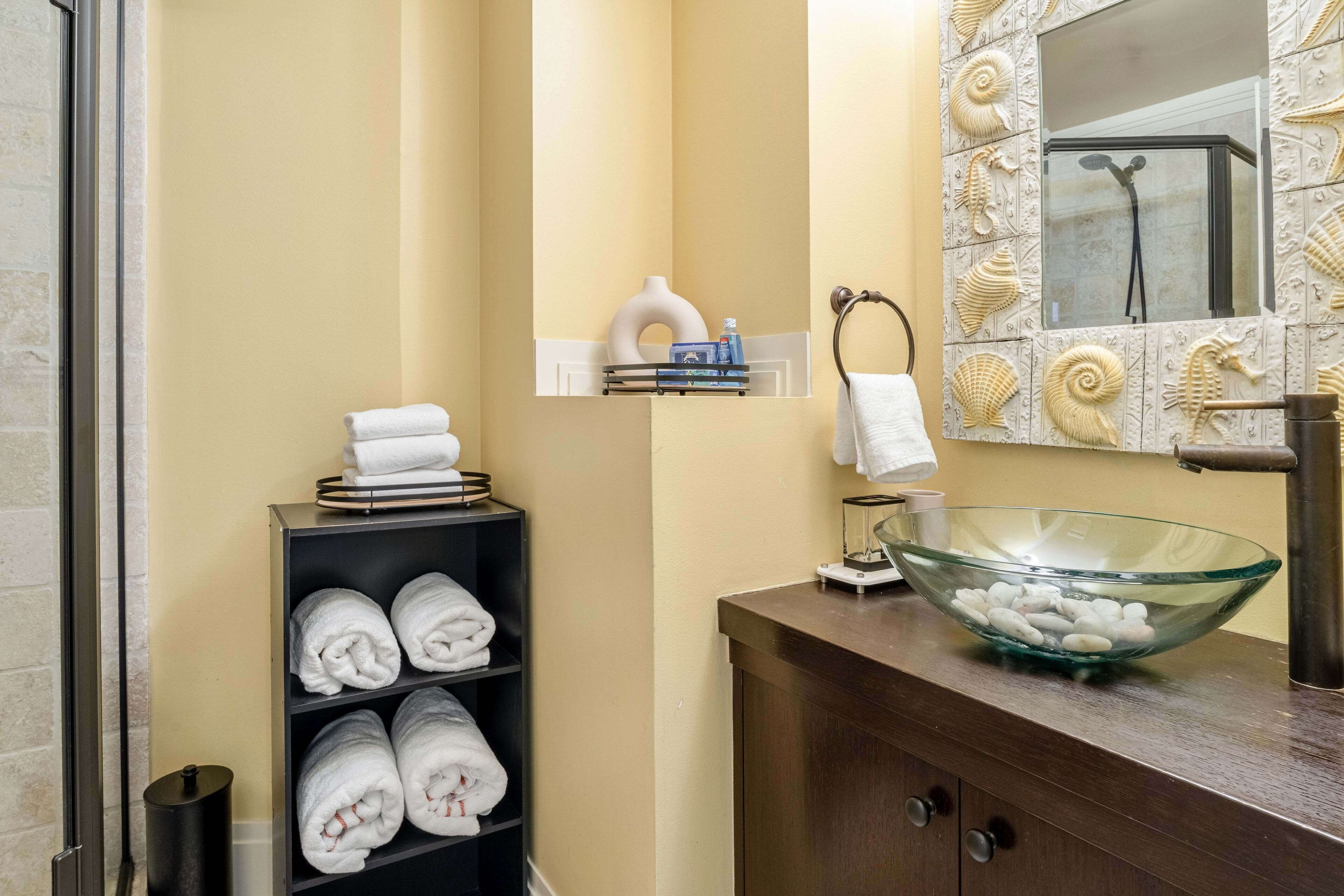 Un bagno con un lavandino in vetro, un portasciugamani e uno scaffale con articoli da toilette.