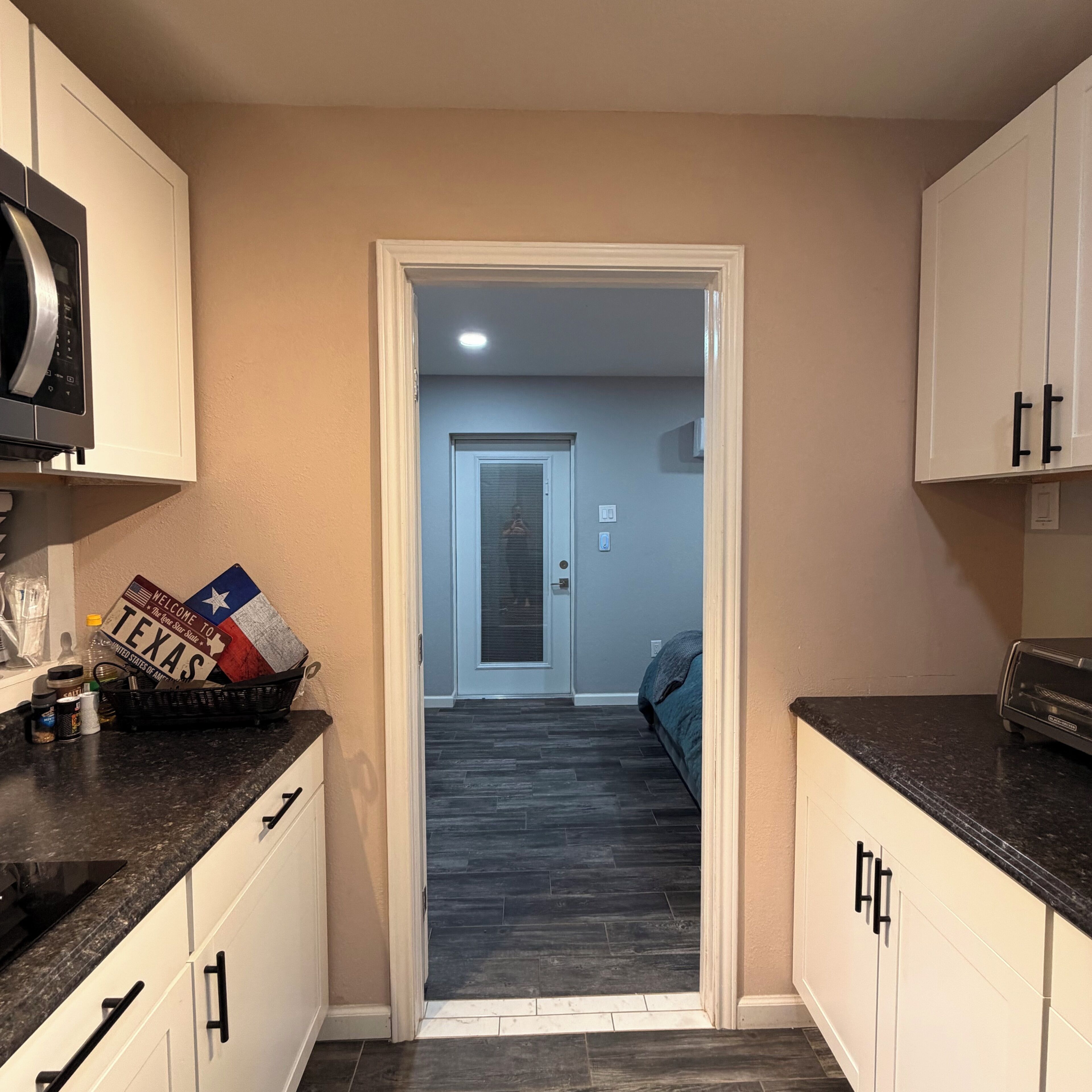 A kitchen with white cabinets, a microwave, and a toaster. A Texas welcome sign is visible on the counter.