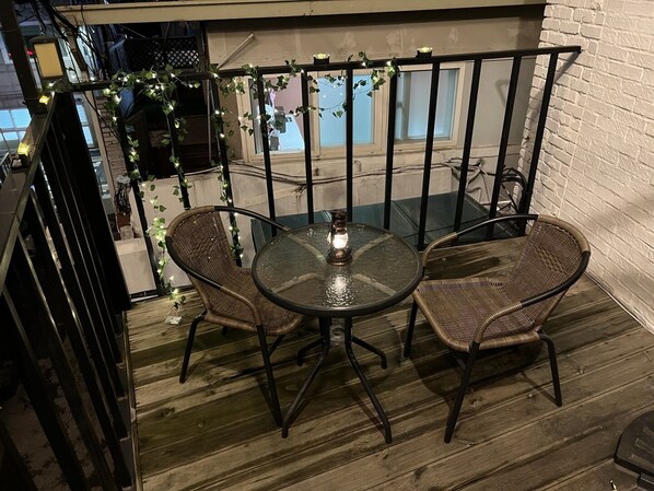 Ein Balkon mit rundem Glastisch und zwei Korbstühlen, verziert mit Lichterketten.