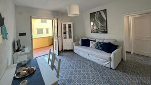 Una stanza con un tavolo da pranzo apparecchiato con piatti e tazze, un divano bianco con cuscini blu, un grande quadro astratto appeso al muro e piastrelle a motivi decorativi.
