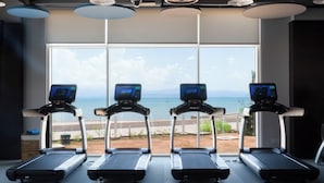 Four treadmills aligned in a row with a large window in the background.