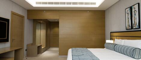 A modern hotel room with a large bed, a flat-screen TV, a wooden wardrobe, and a painting on the wall.