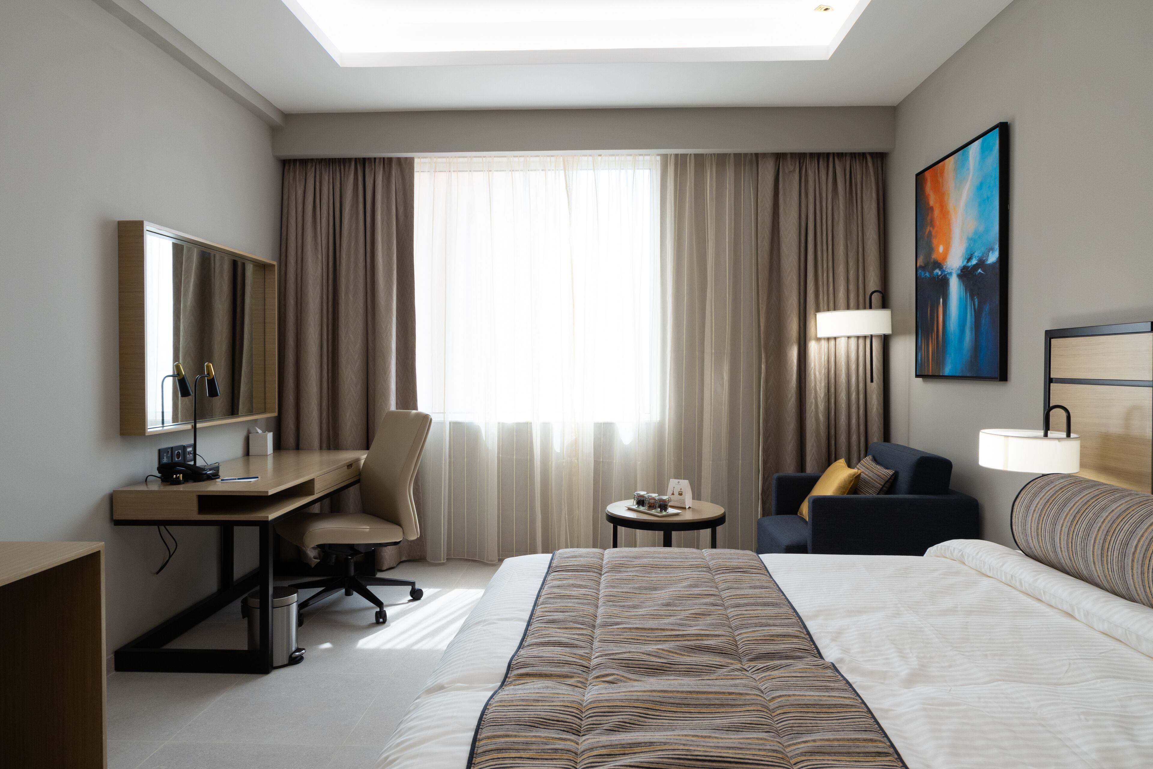 Una habitación de hotel con una cama grande, un escritorio, una silla, una mesita y una lámpara.