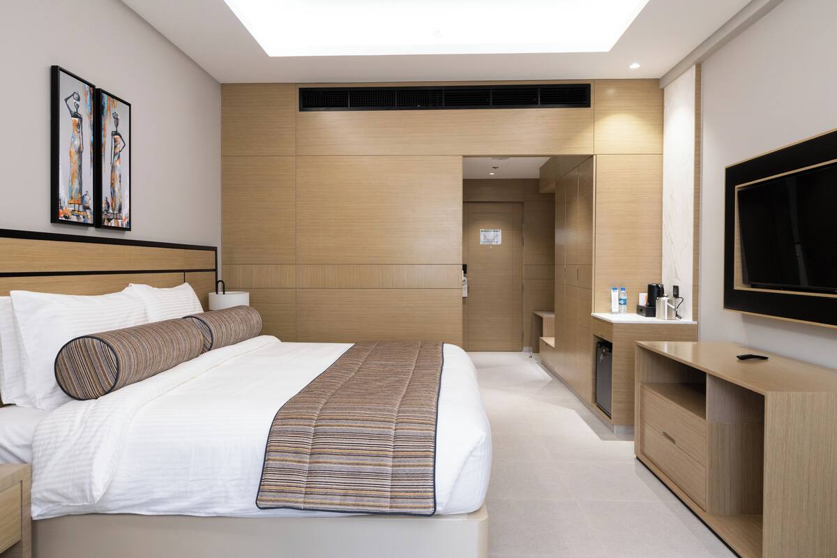 Une chambre d’hôtel moderne dotée d’un grand lit, d’un téléviseur à écran plat, d’un bureau et d’une salle de bain visible à travers une porte ouverte.