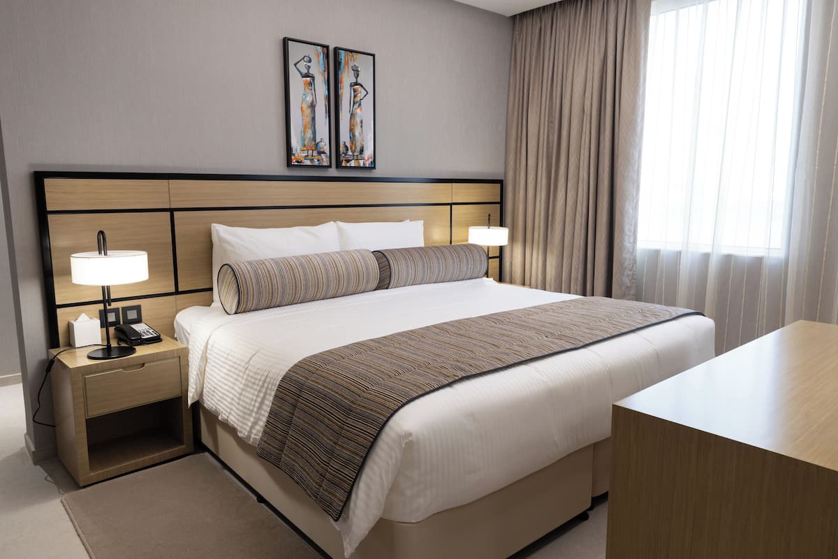 Une chambre d’hôtel avec un grand lit, deux lampes de chevet, une table de chevet avec un téléphone, un bureau et une fenêtre avec des rideaux.