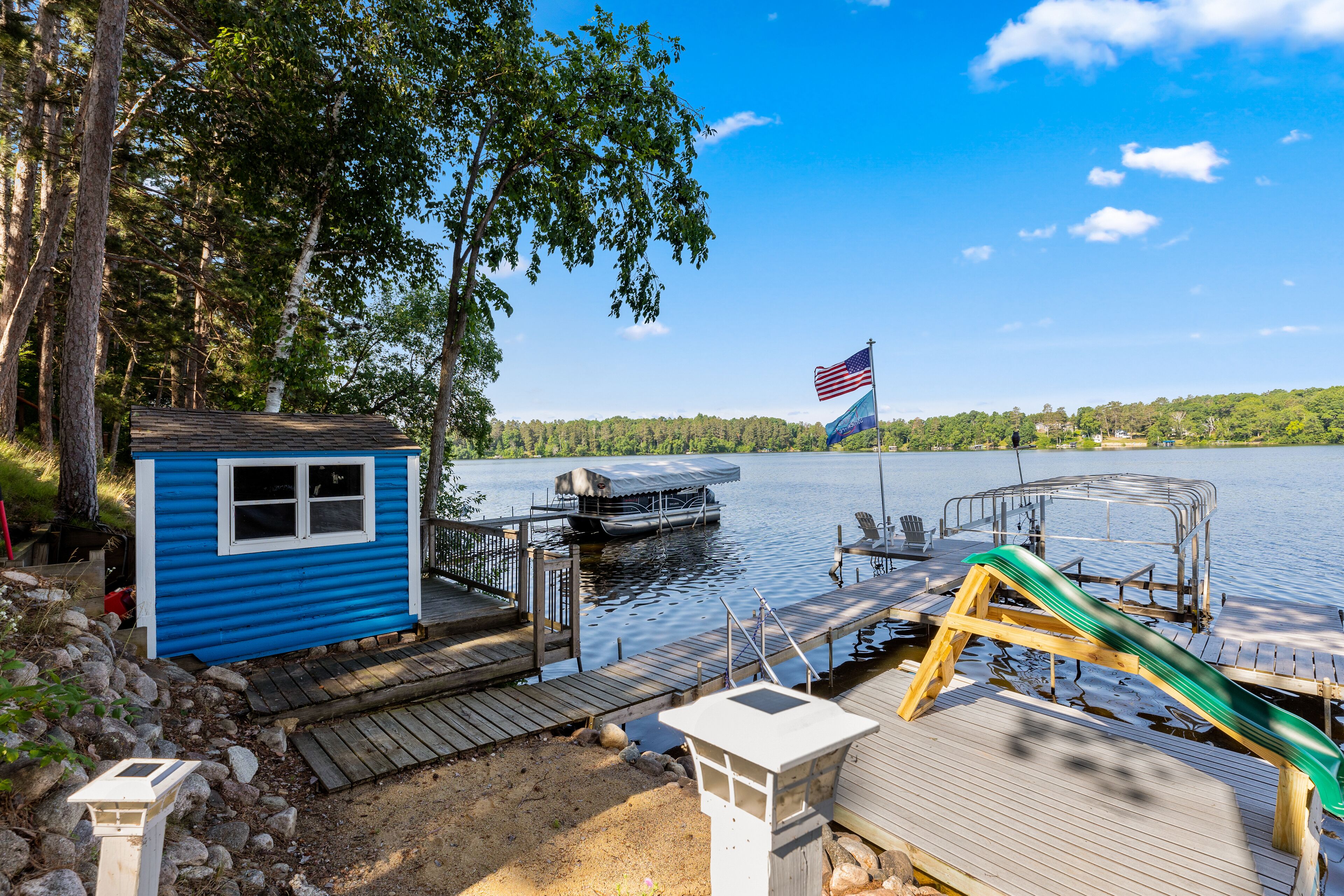 A dock with a small blue shed, a green slide, and a boat on the water.