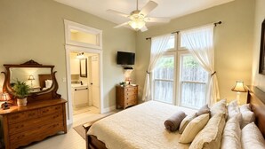 Un dormitorio con una cama, un aparador, un televisor y un ventilador de techo.