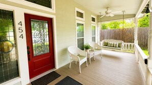 Un porche cubierto con una puerta roja, muebles de mimbre blancos y una terraza de madera.