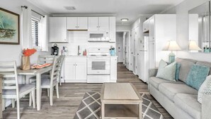 A modern kitchen with white cabinets, a microwave, and an oven. There is a dining area with a table and chairs, and a living area with a sofa and a lamp. - Beachfront Villa W/ Pool & Tennis Hilton Head (Hilton Head Island)