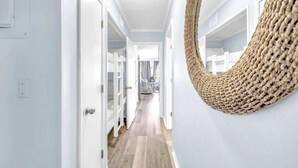 A hallway with white walls, wooden flooring, and a woven wall hanging. - Beachfront Villa W/ Pool & Tennis Hilton Head (Hilton Head Island)