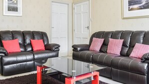 A living room with two black leather sofas, a glass coffee table, and a red accent table. There are two doors and a framed picture on the wall. - 2 bedroom accommodation in Whitby (Whitby)