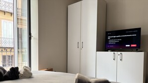 Ein Schlafzimmer mit Bett, Kissen, einem Fernseher auf einem Schrank und einem Fenster mit Blick auf einen Balkon.