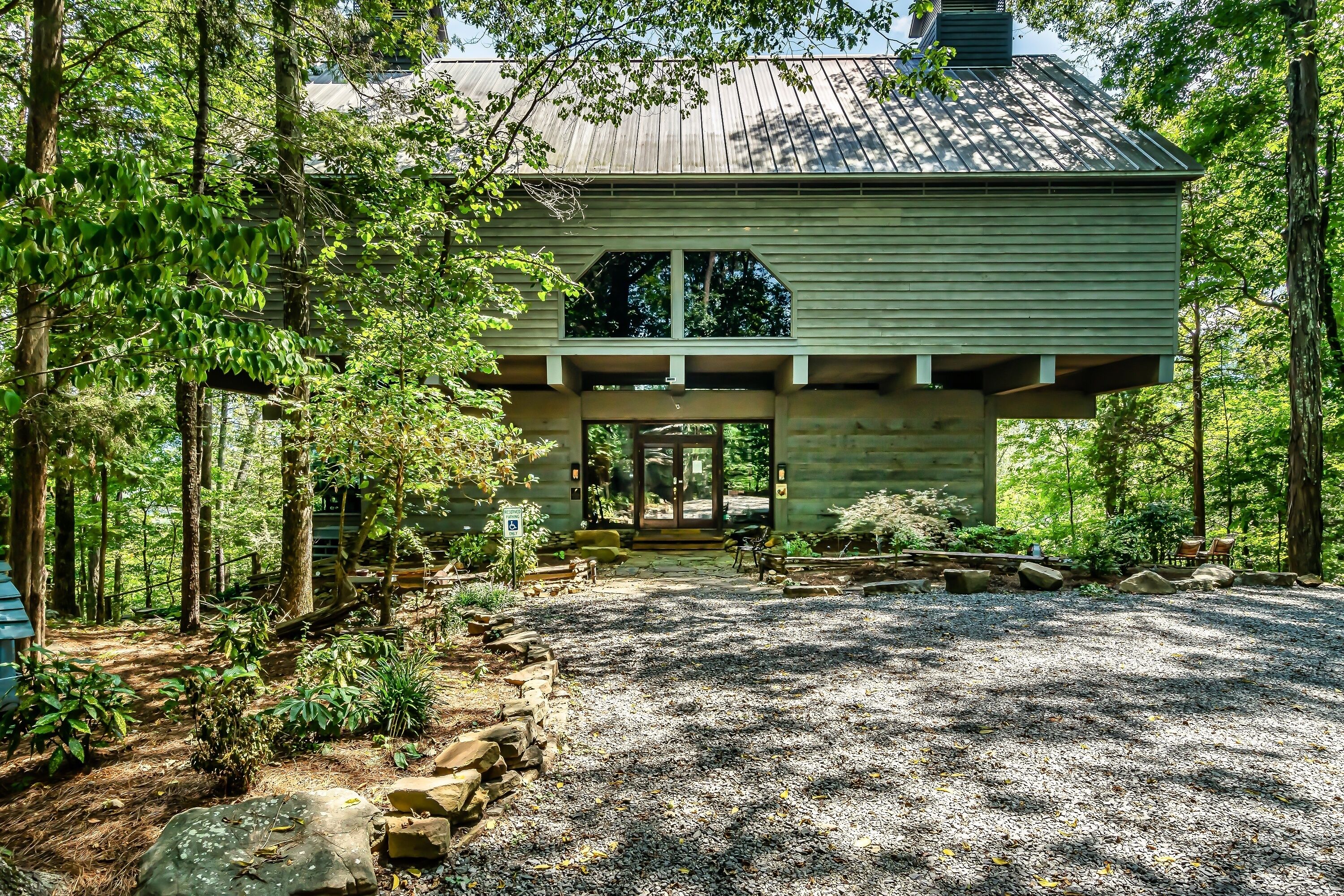 A rustic cabin with a gravel driveway, surrounded by trees and a wooden deck.