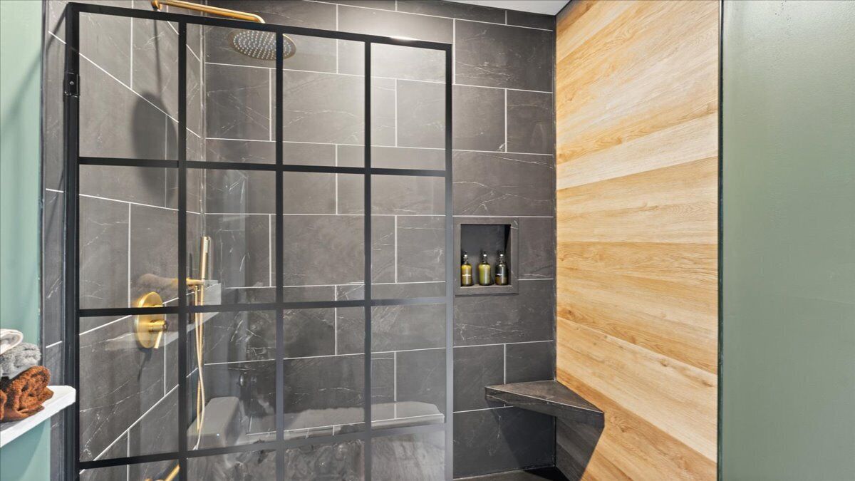 A modern bathroom with a glass-enclosed shower, dark tiled walls, and a wooden accent wall.