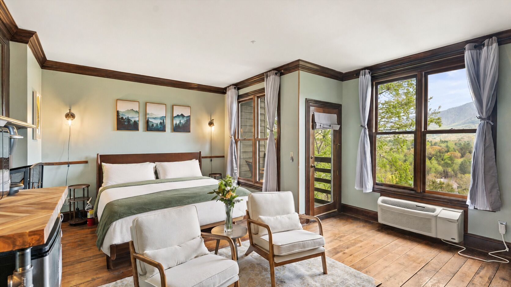 A bedroom with a bed, two chairs, a table, a window with curtains, and a radiator.
