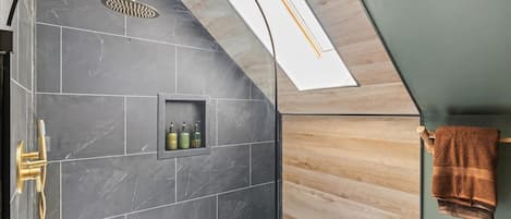 A modern bathroom with a shower, a built-in shelf with toiletries, and a towel rack.