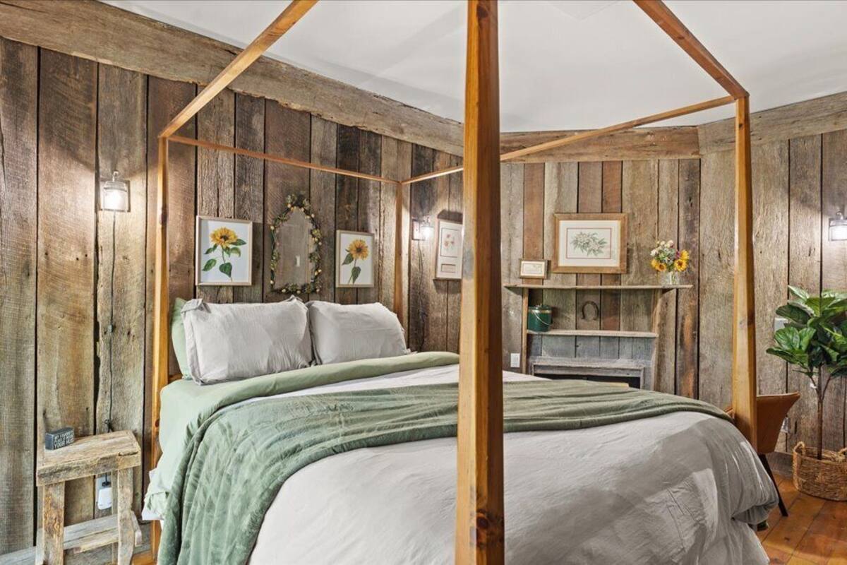A rustic bedroom with a four-poster bed, wooden walls, and a small shelf with decorative items.