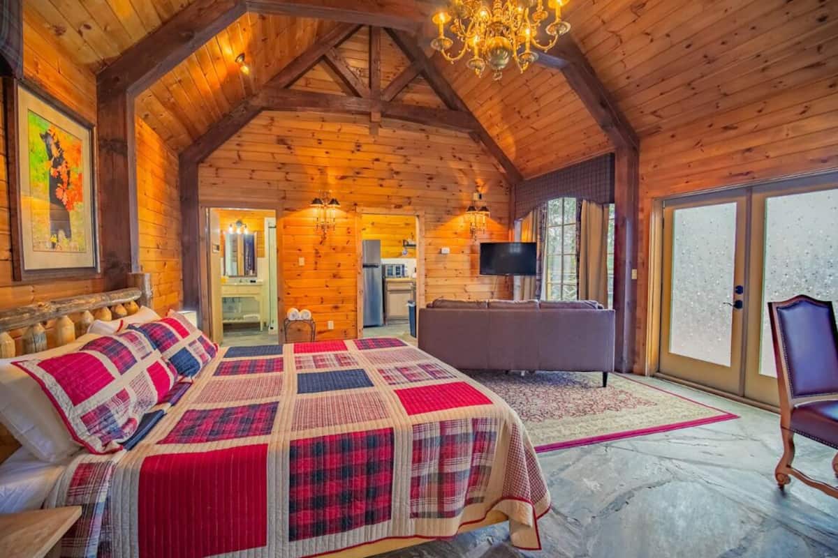 A log cabin room with a large bed, a sofa, a TV, and a chandelier.