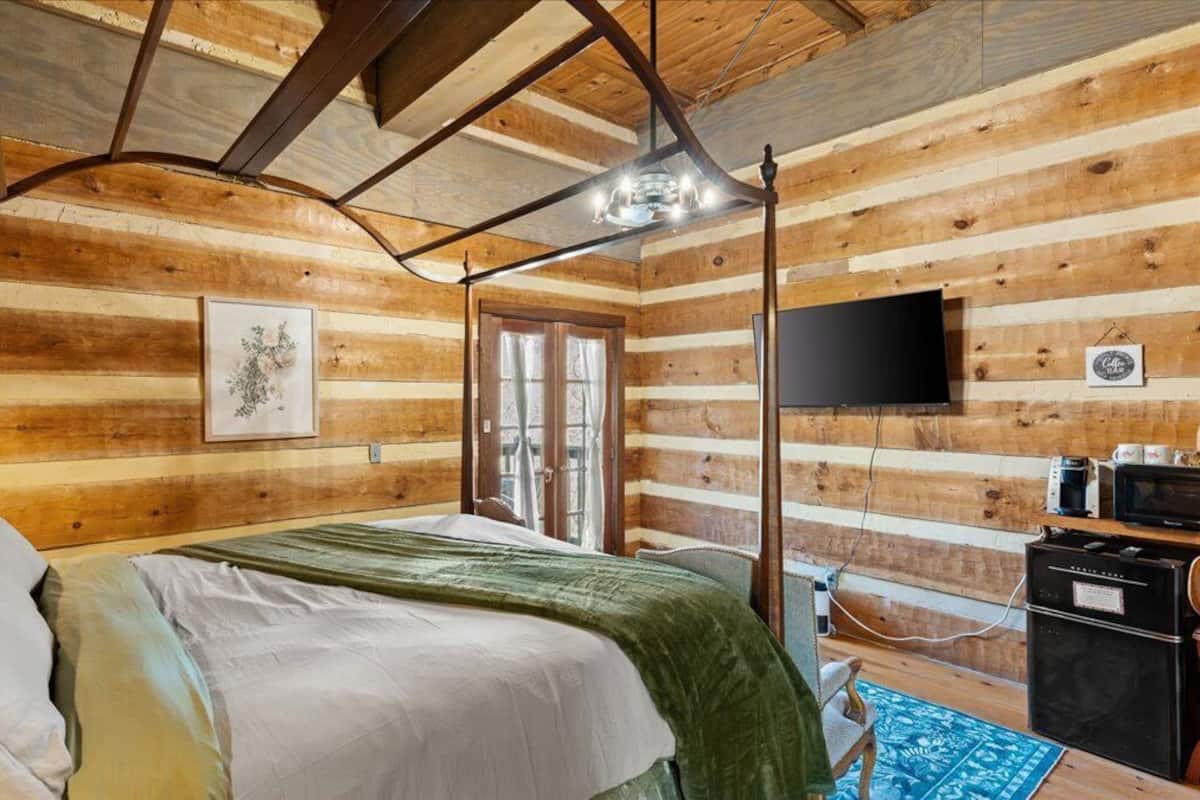 A wooden cabin bedroom with a bed, a desk, a TV, and a window.