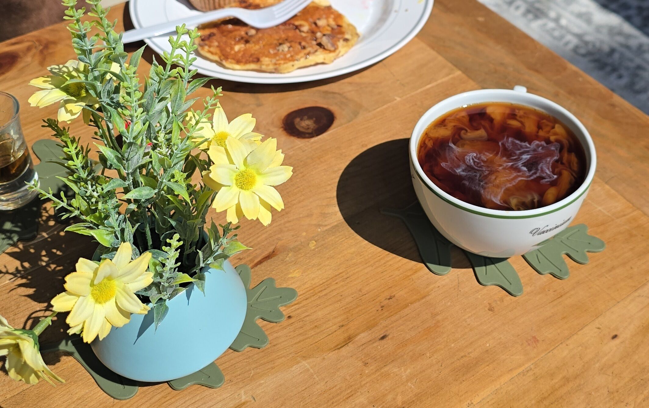 A table with a blue flower vase, a cup of iced tea, and a plate with food.