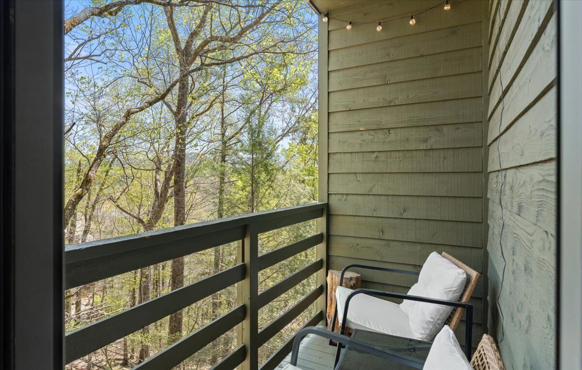 A balcony with a metal railing, a single white cushioned chair, and a string of lights.