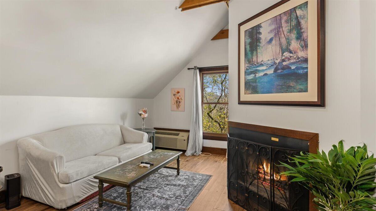 A cozy living room with a white sofa, a fireplace, and a painting of a forest scene.