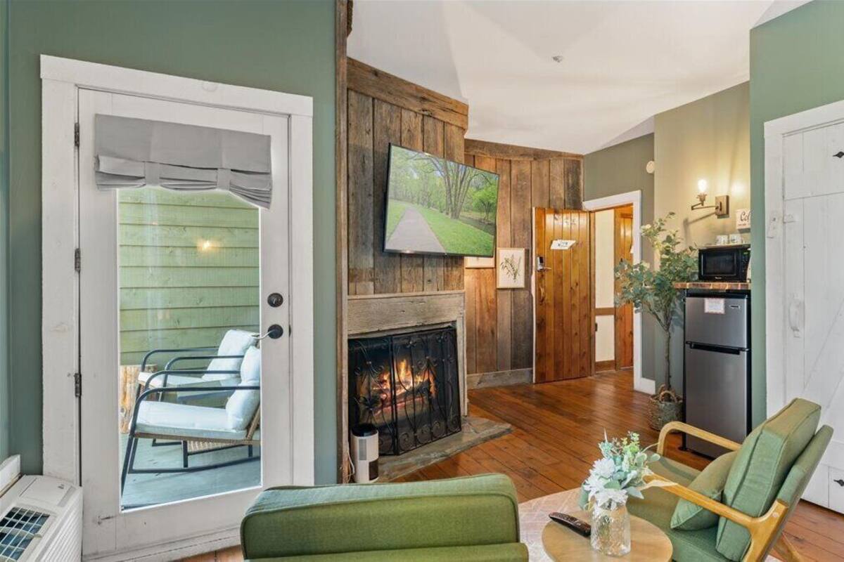 A cozy living room with a fireplace, green walls, and a dining area with a table and chairs.