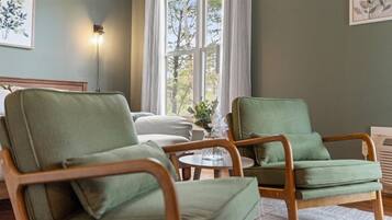 A room with two green armchairs, a small round table, and a bed in the background.