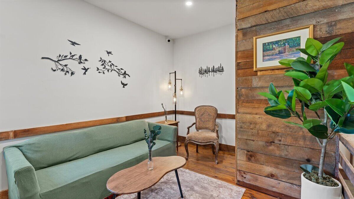 A cozy living room with a green sofa, a wooden coffee table, a vintage armchair, and a potted plant.