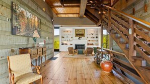 Un interior rústico con una escalera de madera, una chimenea y una estantería llena de libros y objetos decorativos.