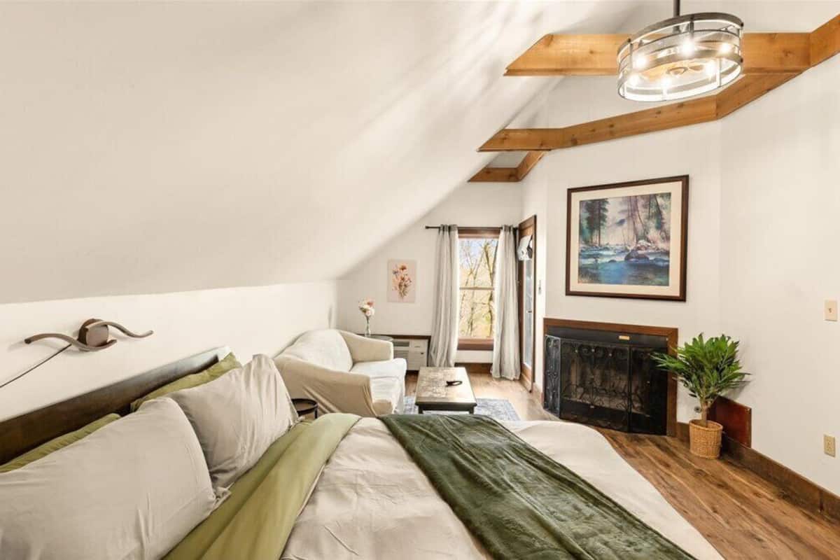 A cozy attic bedroom with a bed, a fireplace, and a large window.