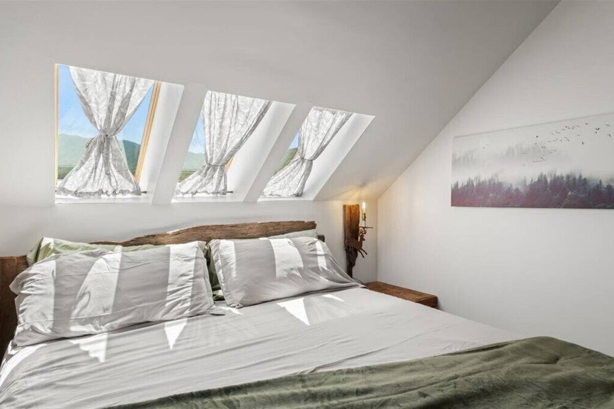 A bedroom with a large bed, skylights, a painting, and a nightstand.