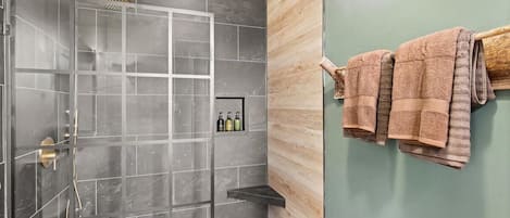 A modern bathroom with a shower, a towel rack, and a shelf with toiletries.