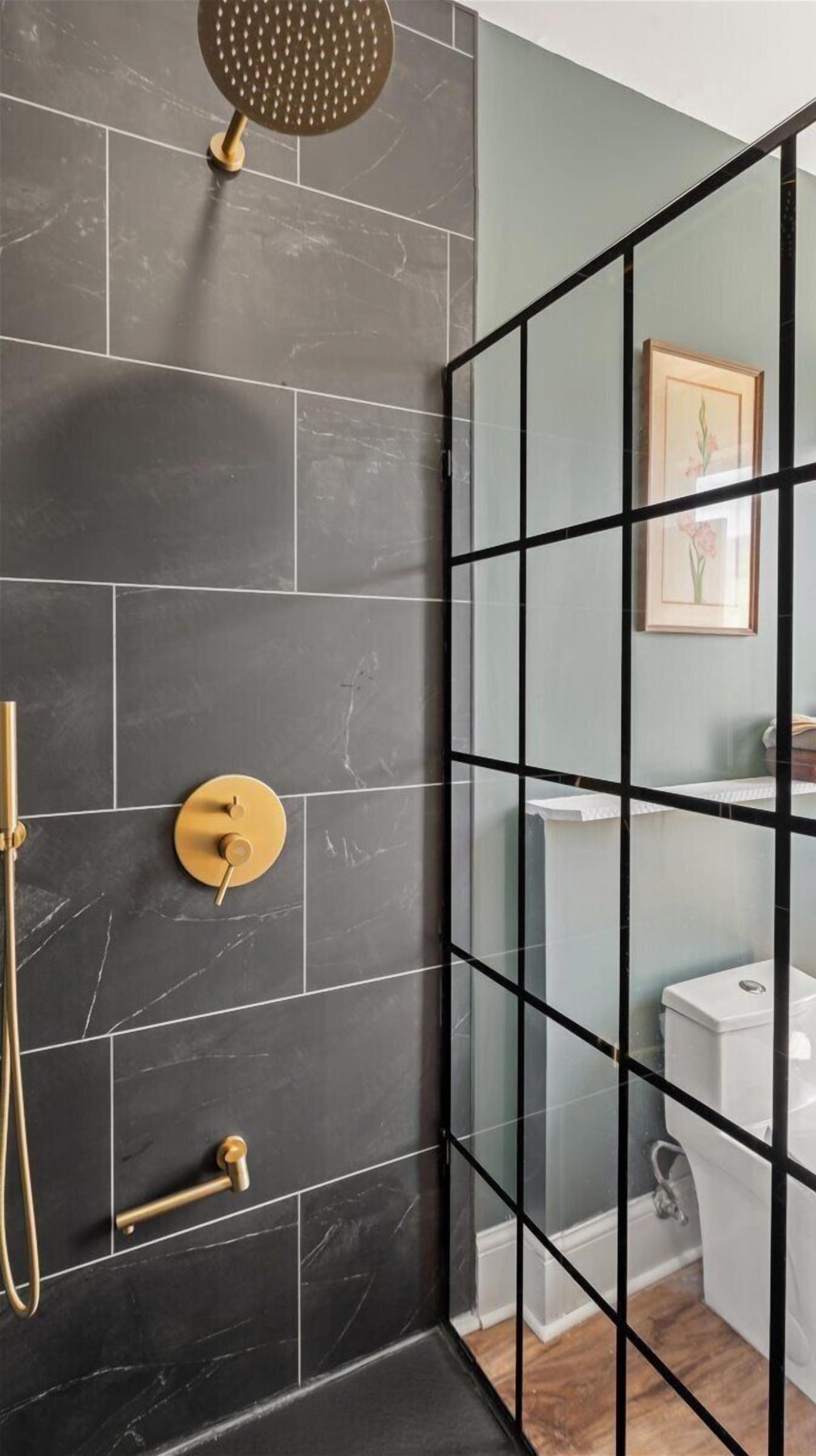 A shower with a glass enclosure, dark marble tiles, and gold fixtures.