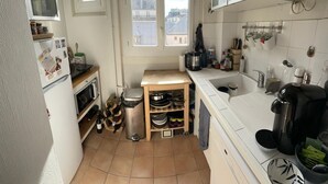 Une cuisine de taille réduite, dotée d’une fenêtre, de meubles blancs, d’un évier et d’une cuisinière.
