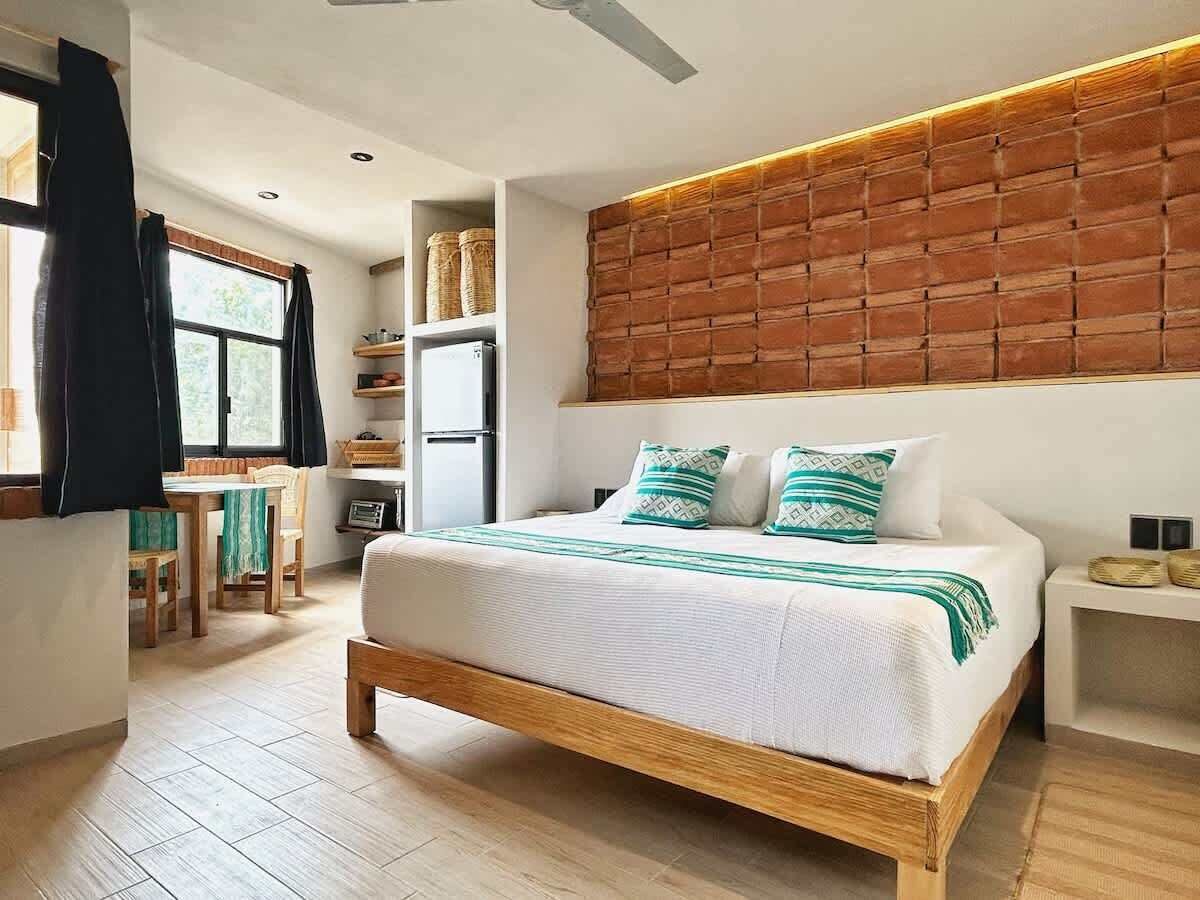 Une chambre moderne avec un lit en bois, une tête de lit ornée d’un motif en briques et un coin repas comprenant une table et des chaises.