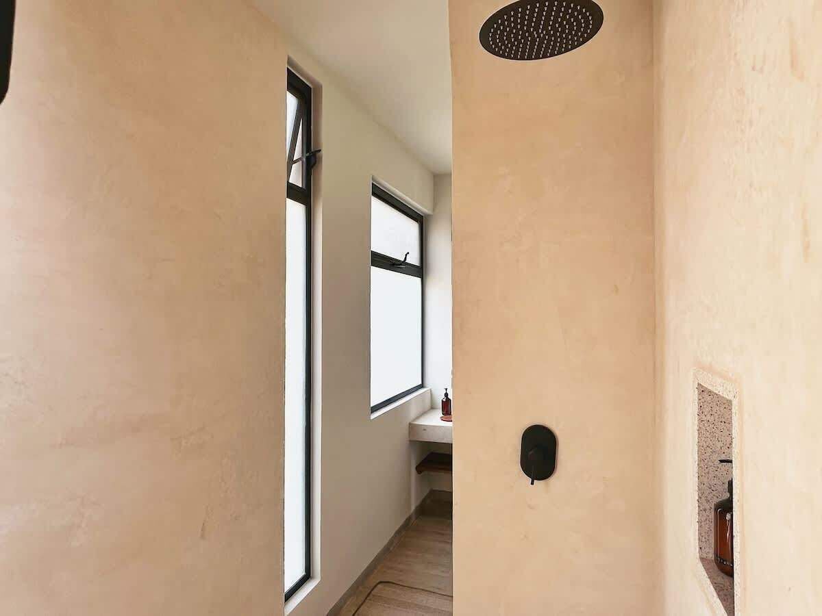 A narrow hallway with beige walls, a window, and a door with a black handle.