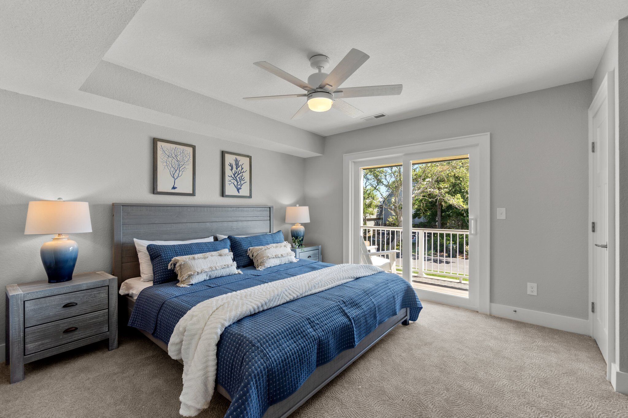 A bedroom with a large bed, two bedside tables with lamps, a ceiling fan, and a view to the outside.