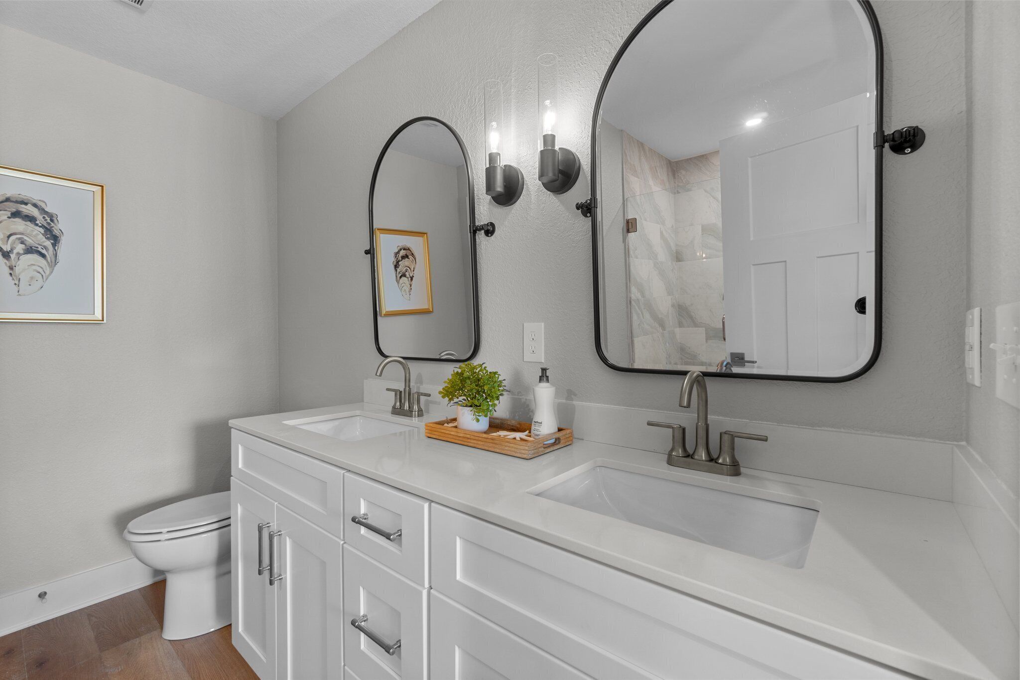 A modern bathroom with a white vanity, two sinks, a toilet, and a large mirror.